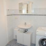 Badezimmer mit Waschmaschine und Spiegel über Waschbecken.