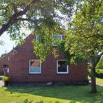 Rotes Backsteingebäude mit grünem Garten und Bäumen im Hintergrund.