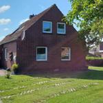 Rotes Backsteingebäude mit Garten und Terrasse unter blauem Himmel.