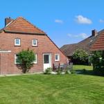 Rotes Backsteingebäude mit Garten und Terrasse unter blauem Himmel.
