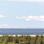 Meer mit Kitesurfern, Strand und Wald im Vordergrund.