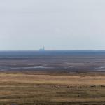 Weite Landschaft mit grasbewachsenem Feld und Küstenbereich im Hintergrund.
