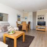 Wohnzimmer mit Sofa, Couchtisch und Fernseher. Essbereich mit Tisch und Stühlen. Holzboden und Spiegel an der Wand.