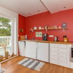 Küche mit roten Wänden, weißen Schränken und Holzoberflächen. Blick auf Balkon mit Blick auf Bäume.