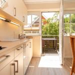 Küche mit Essbereich und Balkon. Tisch und Stühle sind aus Rattan.