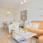 Wohn- und Essbereich mit Sofa, Tisch und Stühlen. Wanddekoration mit Zitat.