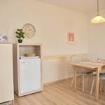 Essbereich mit Tisch, vier Stühlen und Küchenmöbeln. Wanduhr und Pendelleuchte sind sichtbar.