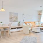 Wohn- und Essbereich mit Sofa, Tisch und Stühlen sowie Pflanzen.