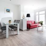 Wohn- und Essbereich mit rotem Sofa, Glas-Tisch und großen Fenstern.