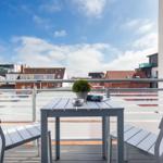 Terrasse mit Tisch und zwei Stühlen, Blick auf Stadtlandschaft unter blauem Himmel.
