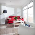 Wohnzimmer mit rotem Sofa, weißem Sessel und großem Fenster.