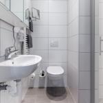 Badezimmer mit Toilette, Waschbecken und Dusche. Weiße Fliesen und graue Bodenfliesen.