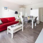 Wohn- und Essbereich mit rotem Sofa, Glas-Tisch und Stühlen.