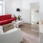 Wohnzimmer mit rotem Sofa, weißem Sessel und Fernseher an der Wand.