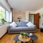 Wohnzimmer mit grauem Sofa, Holzboden und Fenster mit Blick auf Grün.