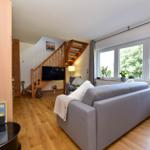 Wohnzimmer mit Sofa, TV und Holztreppe zur oberen Etage.