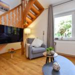Wohnzimmer mit Holztreppe, TV und Fenster mit Blick auf Bäume.