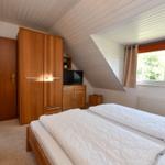 Schlafzimmer mit Doppelbett, Kleiderschrank und TV. Dachschrägen und Fenster mit Blick.