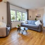 Wohnzimmer mit Sofa, Sessel und Holzboden. Fenster mit Blick auf Grün.