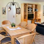 Esszimmer mit Holztisch, Rattanstühlen und integriertem Wohnbereich mit Sofa und TV.