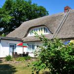 Haus mit Strohdach, Garten und Terrasse mit Sonnenschirm.