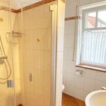 Bad mit Dusche, Waschbecken und Fenster mit Vorhang.