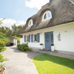 Haus mit Strohdach, blauer Tür und blauen Fensterläden. Vorhof mit Rasen und Kiesweg.