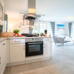 Küche mit weißer Einbauküche und Blick in Wohnzimmer mit Sofa und Kamin.