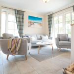 Wohnzimmer mit Sofa, Sesseln und Tisch. Fenster und Vorhänge sind sichtbar.