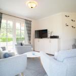 Wohnzimmer mit Sofa, Sessel und TV. Fenster mit Plaidgardinen. Kamin und Wanddekoration.