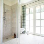 Badezimmer mit Dusche, Toilette und Fenster mit Vorhängen.