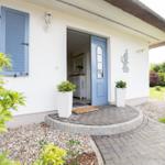 Haus mit blauer Tür und Fensterläden, Eingangsbereich mit Pflanzen und Steinweg.