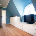 Ein Schlafzimmer mit blauen Wänden, weißem Schrank und Holzboden. TV und Fenster sind sichtbar.