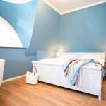 Schlafzimmer mit blauen Wänden, weißem Bett und Holzboden.