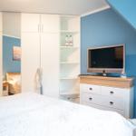 Schlafzimmer mit Doppelbett, Kleiderschrank und Fernseher auf Kommode.