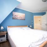 Schlafzimmer mit Dachschrägen, Bett, Nachttisch und Wandbild.