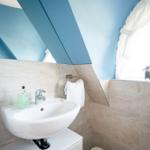 Badezimmer mit Waschbecken, Spiegel und Fenster mit Vogeldekoration.