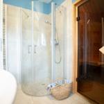 Dusche mit Glaswand und Sauna mit Holztüren.