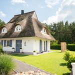 Haus mit Strohdach, blauer Tür und grünem Garten vor Wald.