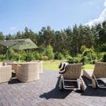 Terrasse mit Rattanmöbeln, Sonnenschirm und Blick in den Wald.
