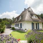 Haus mit Strohdach, blauen Fensterläden und gepflegtem Garten mit Lavendel.