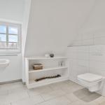 Badezimmer mit Fenster, Waschbecken, Toilette und Regal