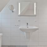 Badezimmer mit Waschbecken, beleuchtetem Spiegel und Haken an der Wand.