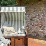 Strandkorb mit Kissen und Buch auf Terrasse neben Backsteinwand.