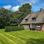 Haus mit strohgedecktem Dach, Garten und Terrasse mit Gartenmöbeln.