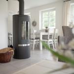 Wohn- und Essbereich mit Kaminofen, Tisch, Stühlen und Fenstern.