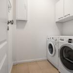 Waschmaschine und Trockner in einem hellen Raum mit weißen Schränken und Fliesenboden.