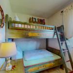 Zimmer mit Doppelstockbett, Nachttisch und Lampe. Fenster mit Vorhängen.