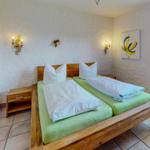 Zimmer mit Doppelbett, Holzgestell, grünen Matratzen und zwei Nachttischen.