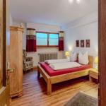 Schlafzimmer mit Holzbett, Kleiderschrank und Fenster mit Vorhängen.